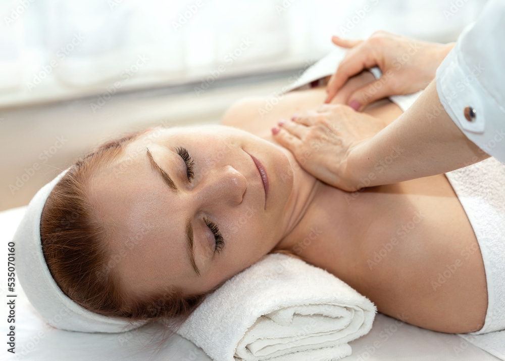 Hands of a massage therapist in a beauty salon performing a cleansing procedure. A young pretty woman with closed eyes lies relaxed on a massage table on a white bedspread and covered with a white