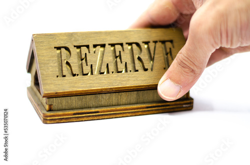 Table reservation letter. Human hand holding reservation sign. Wooden reservation drawn from the back on an isolated white background.
