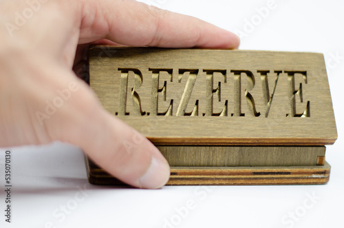 Table reservation letter. Human hand holding reservation sign. Wooden reservation drawn from the back on an isolated white background.
