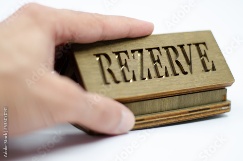 Table reservation letter. Human hand holding reservation sign. Wooden reservation drawn from the back on an isolated white background.

