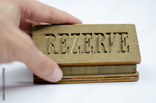 Table reservation letter. Human hand holding reservation sign. Wooden reservation drawn from the back on an isolated white background.
