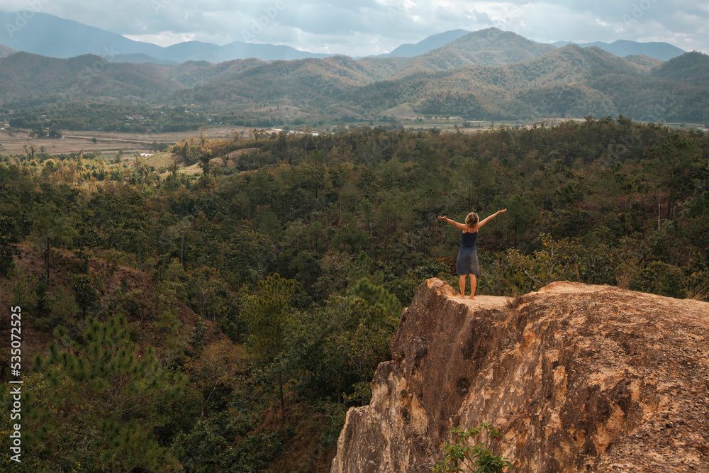 A girl with her hands raised stands on the edge of a canyon in northern Thailand.