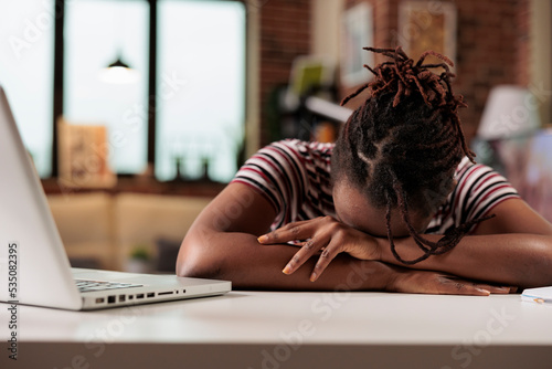 Overworked freelancer sleeping on table at daytime, sleepy stressed remote worker, professional burnout. Tired student lying on desk, exhausted african american employee having break at workplace