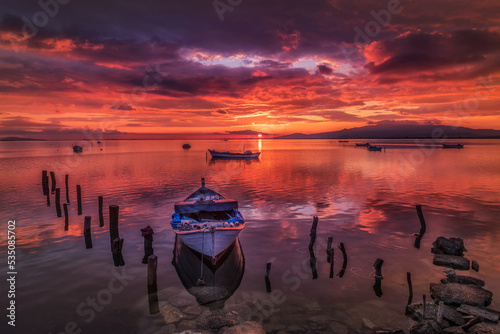 Solo fisher boat on foreground and colorful sunset sky on background 