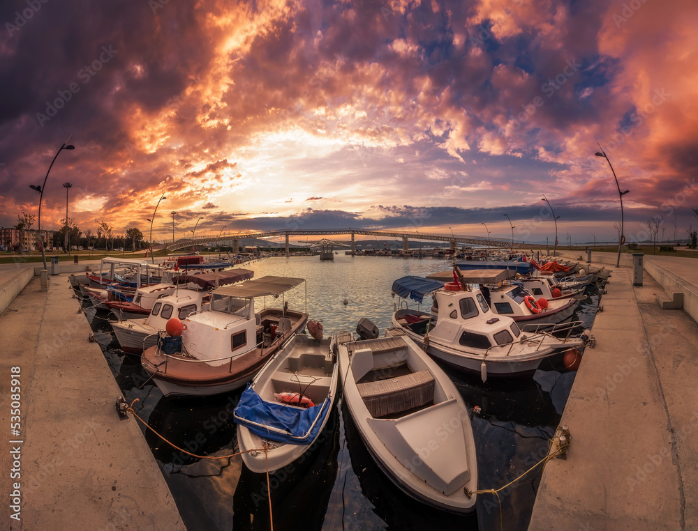 Boats on harbour win a panoramic shot, boats on foreground burning colorful sky on background