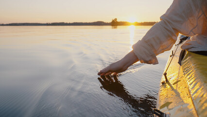 Person sails on canoe touching water with hand making waves