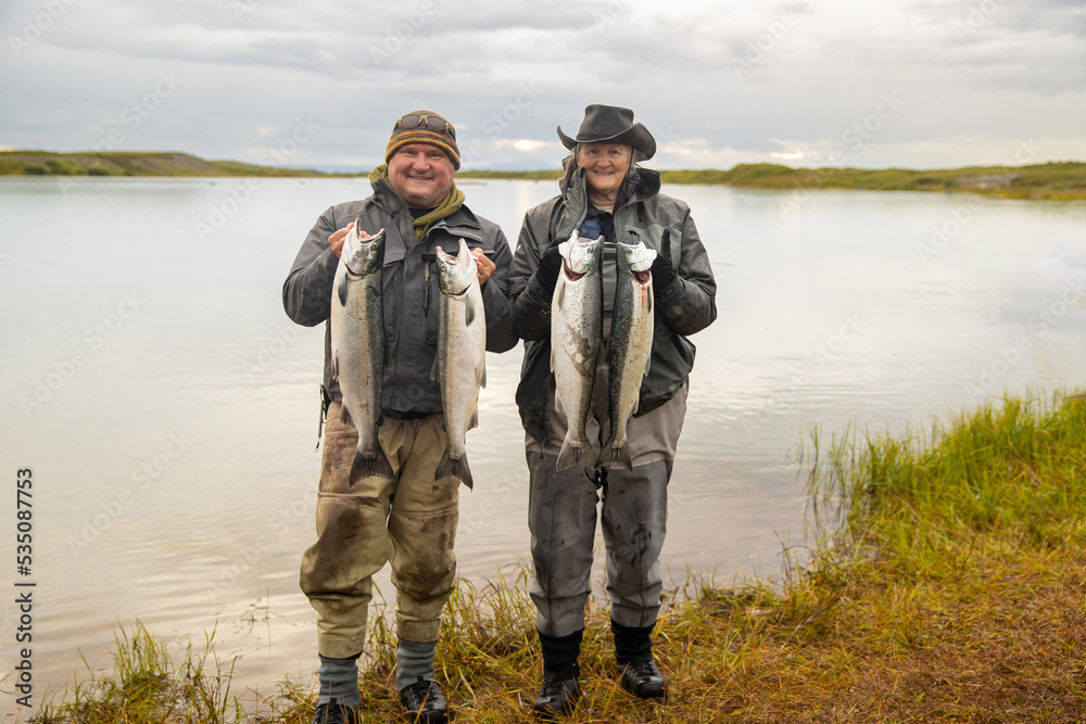 Happy man and woman holding two large coho salmon each on the bank of the Egegik river in Alaska Happy man and woman holding two large coho salmon each on the bank of the Egegik river in Alaska