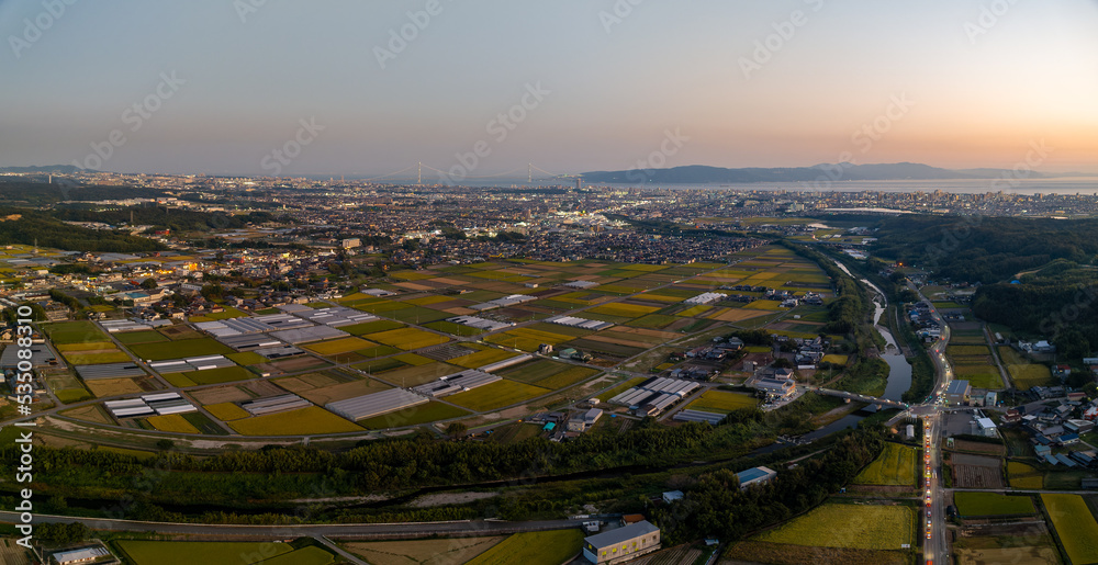 Panoramic aerial view of coastal farms and lights from city at sunset