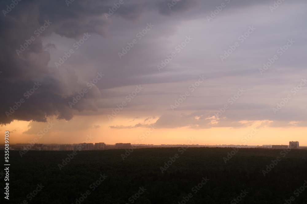 Stormy sky at sunset with dark rain clouds. Rain over a summer forest with green trees