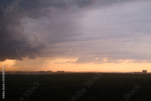 Stormy sky at sunset with dark rain clouds. Rain over a summer forest with green trees