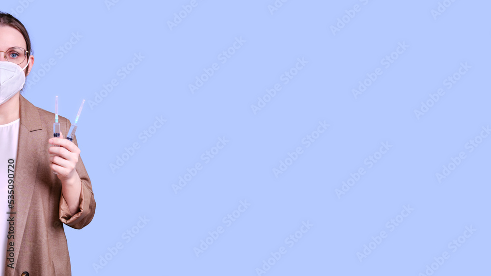 Woman teacher in medical face mask holds syringes for vaccination on studio purple background, banner copy space