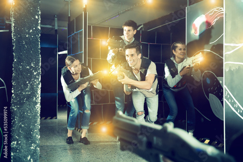Cheerful guy with laser pistol playing laser tag with friends on dark room © JackF