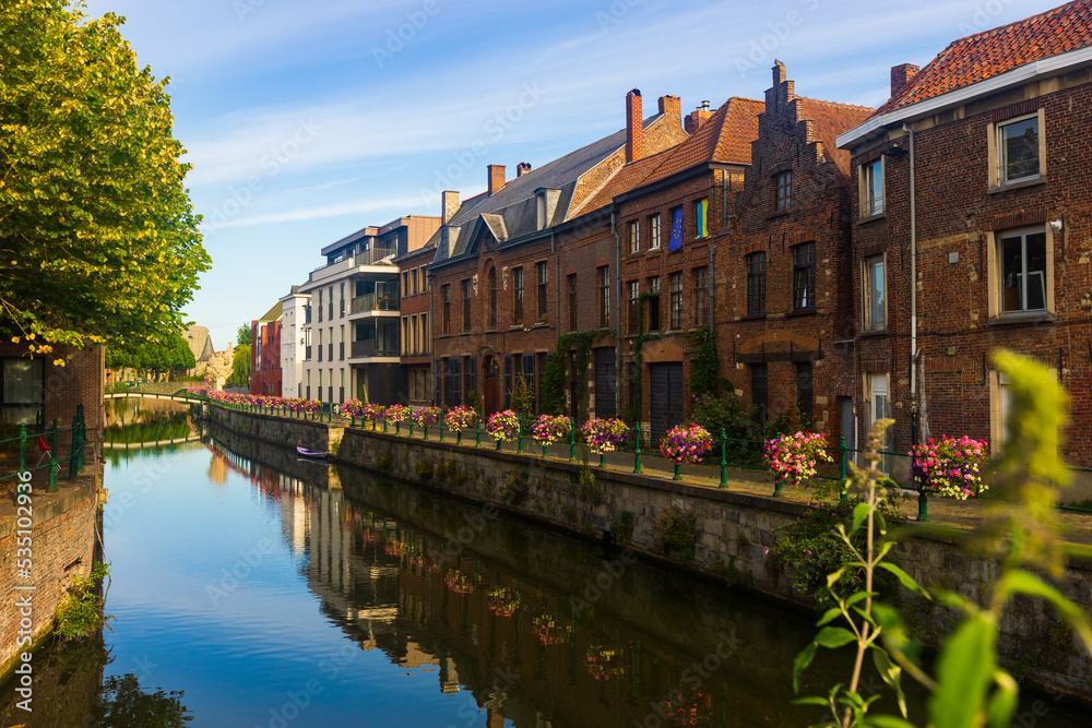 Scenic cityscape of Ghent with traditional Flemish style brick townhouses decorated with colorful blooming flowers on banks of Leie river on sunny summer day, Belgium..