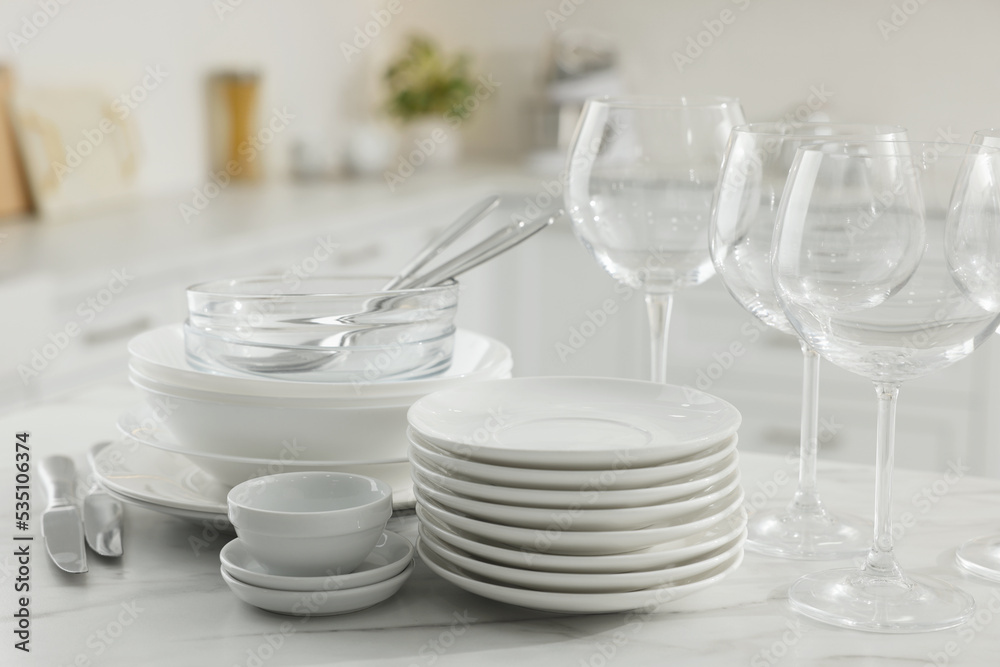 Different clean dishware, cutlery and glasses on white marble table in kitchen
