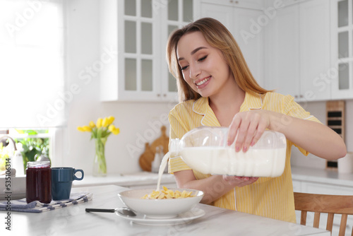 Young woman pouring milk from gallon bottle into plate with breakfast cereal at white marble table in kitchen