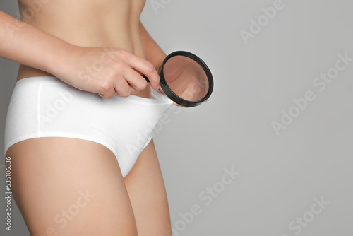 Woman examining genital herpes with magnifying glass on light grey background, closeup. Space for text photo