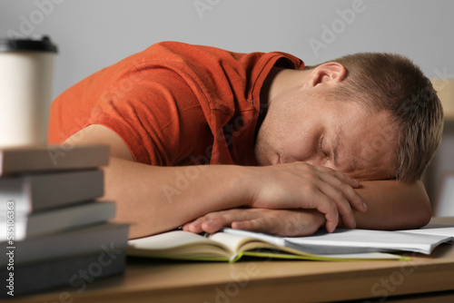 Foto Tired man sleeping near books at wooden table indoors