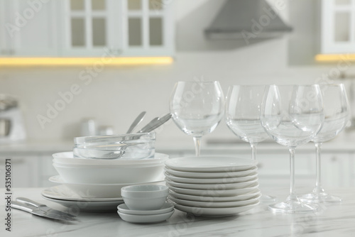 Different clean dishware, cutlery and glasses on white marble table in kitchen