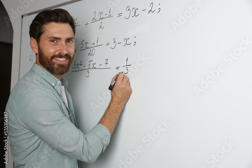 Happy teacher explaining mathematics at whiteboard in classroom