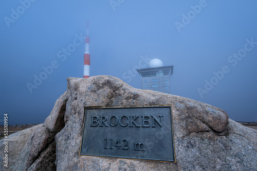 Schild mit Höhenangaben des Brocken, mit Fernsehturm und Brockenhotel im Hintergrund