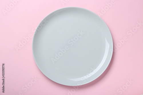 Empty ceramic plate on pink background, top view