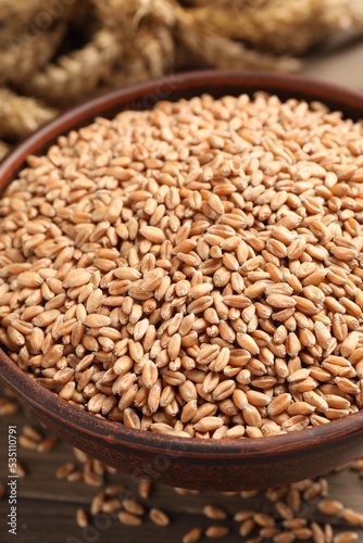 Wheat grains in bowl on wooden table, closeup