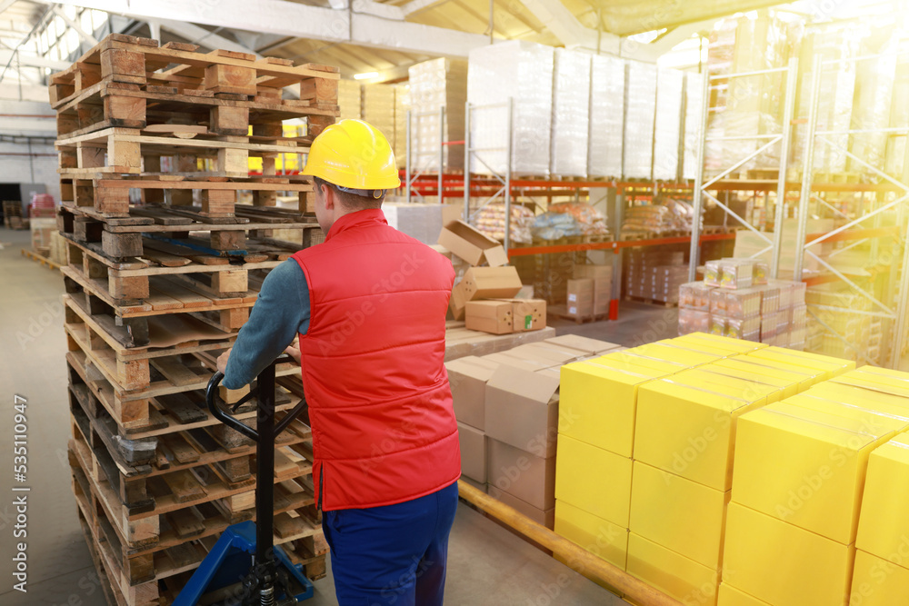 Worker moving wooden pallets with manual forklift in warehouse, back view Worker moving wooden pallets with manual forklift in warehouse, back view