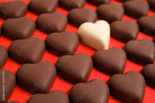 Tasty heart shaped chocolate candies on red background, closeup. Happy Valentine's day
