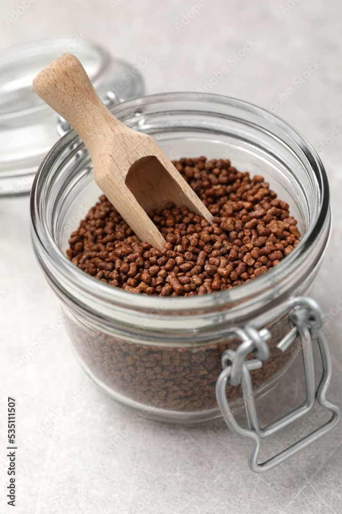 Glass jar with wooden scoop and buckwheat tea granules on light grey table, closeup Glass jar with wooden scoop and buckwheat tea granules on light grey table, closeup