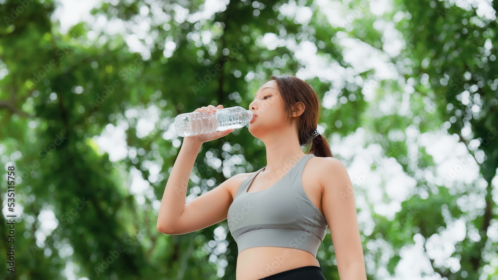 Young asian woman drinking water from a bottle while taking a break during her workout. Happy adolescence female working out in the park and taking rest a break to drink water Young asian woman drinking water from a bottle while taking a break during her workout. Happy adolescence female working out in the park and taking rest a break to drink water