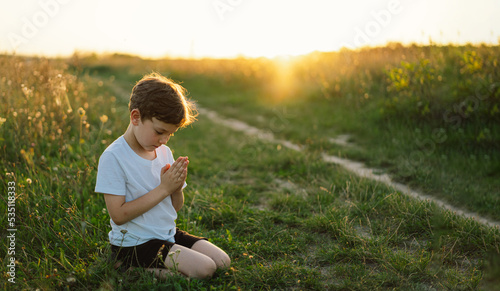 Boy closed her eyes and praying in a field at sunset. Hands folded in prayer concept for faith, spirituality and religion.