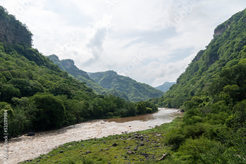 dirty river seen through the huentitan ravine in guadalajara, green vegetation, trees, plants and mountains, mexico photo