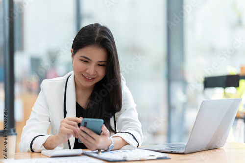Asian businesswoman in formal suit in office happy and cheerful during using smartphone and working.