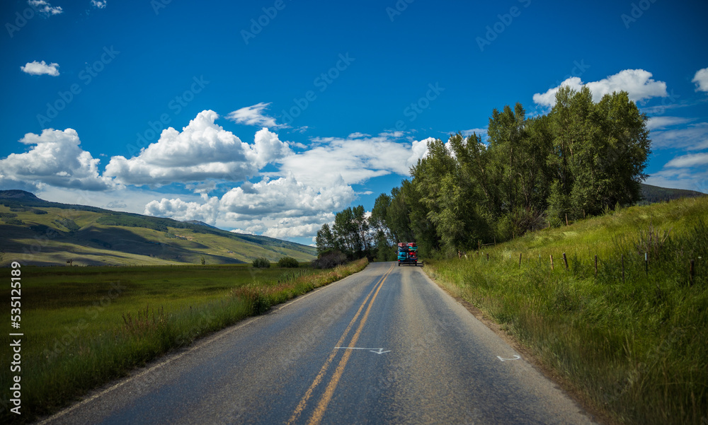 Road to to the summer mountains with green trees and sunlit hills