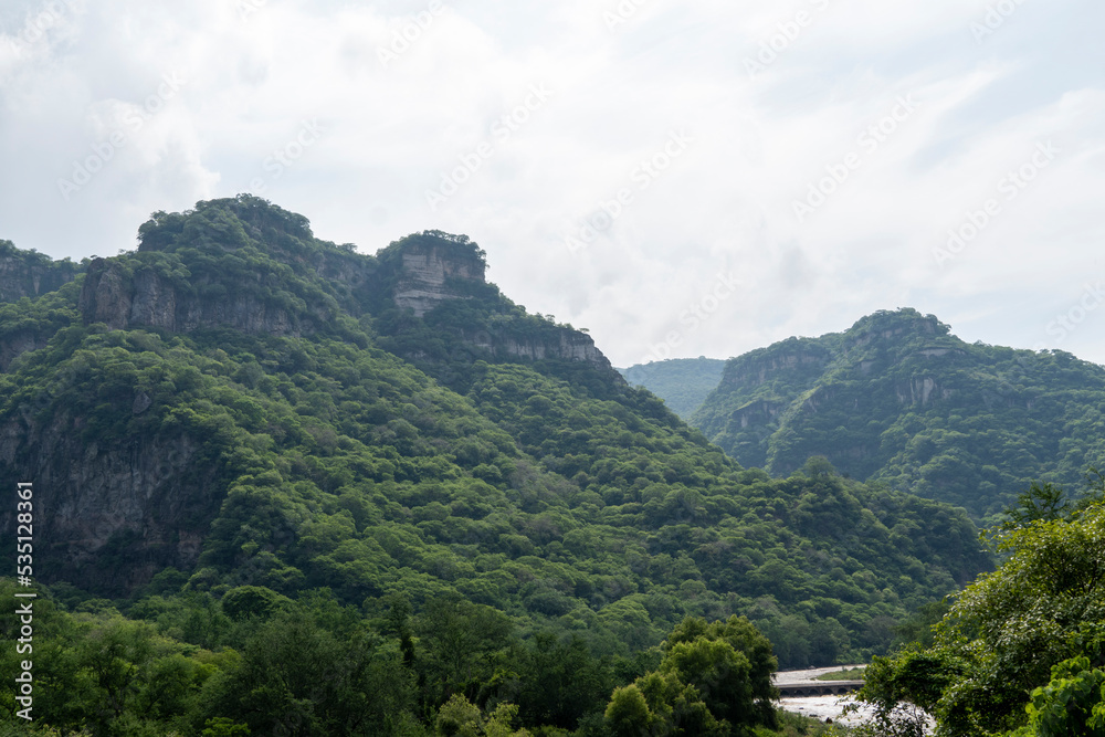 dirty river seen through the huentitan ravine in guadalajara, green vegetation, trees, plants and mountains, mexico