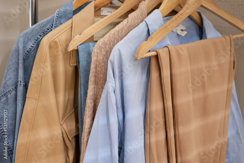 Trendy capsule wardrobe in beige and light blue on a rail rack. Shadow from the blinds on the beige wall and copy space.