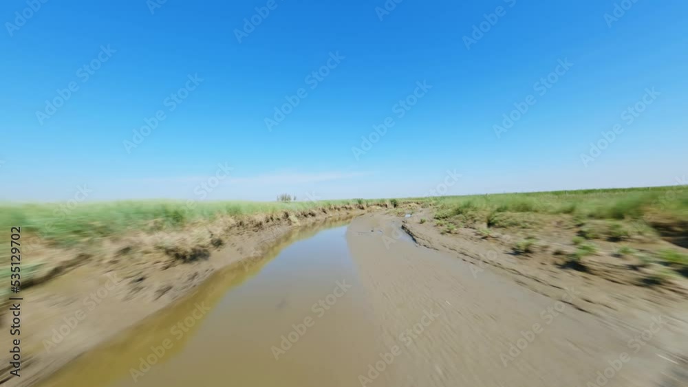 FPV drone shot flying low over a broad, muddy ditch underneath a clear blue summer sky in a nature reserve in Zeeland, the Netherlands FPV drone shot flying low over a broad, muddy ditch underneath a clear blue summer sky in a nature reserve in Zeeland, the Netherlands