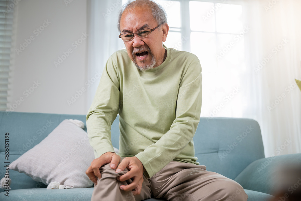 Old man suffering from knee joint pain on sofa living room, bone pain in elderly at home, senior man knee problem painful, unhappy old age hand holding on knee pain after tendon surgery Old man suffering from knee joint pain on sofa living room, bone pain in elderly at home, senior man knee problem painful, unhappy old age hand holding on knee pain after tendon surgery