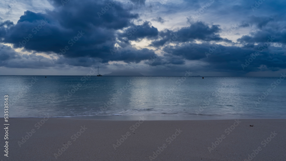 Obraz premium A quiet evening on a tropical beach. The turquoise ocean is calm. Clean smooth sand on the shore. Picturesque blue clouds in the sky. Seychelles. Mahe. Beau Vallon
