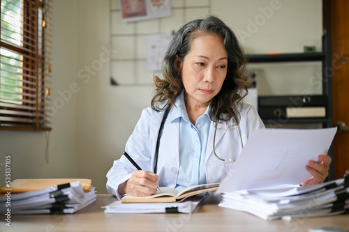 Professional aged Asian female doctor contracting on reading a medical research paper