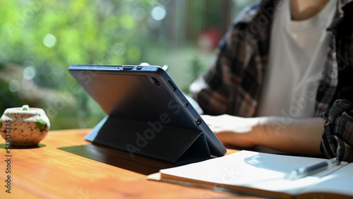 Young Asian female freelancer remote working at the cafe, using tablet. cropped image