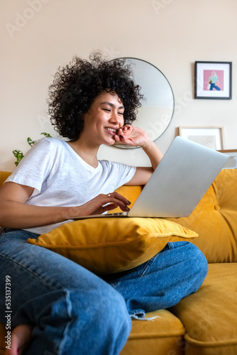 Happy African American woman having fun using laptop at home. Laughing watching funny online videos.