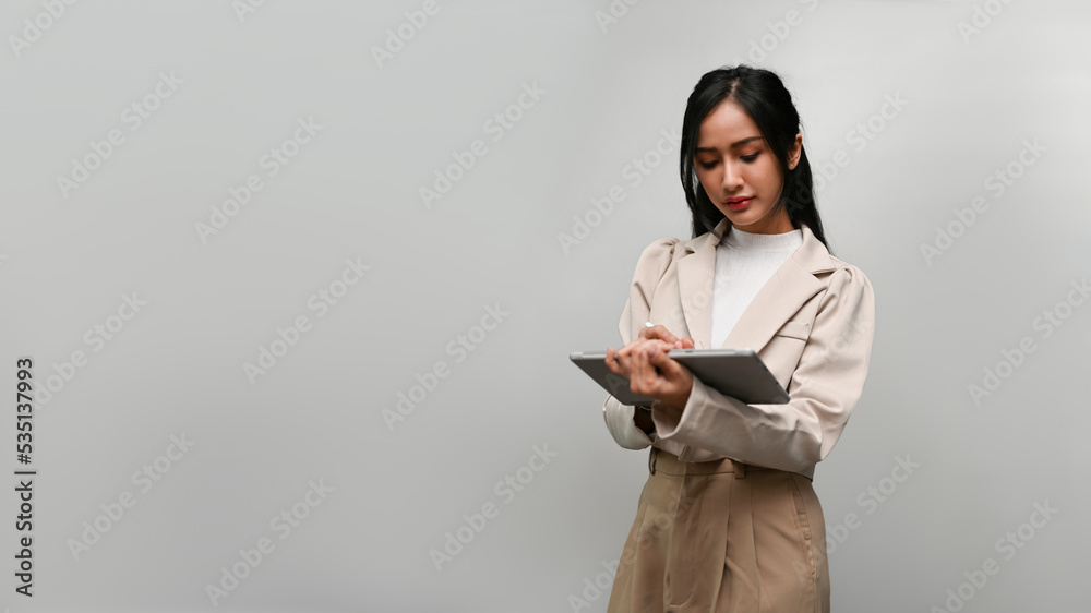 Asian female or businesswoman, using tablet, standing isolated over grey background Asian female or businesswoman, using tablet, standing isolated over grey background