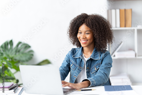 Cheerful african american woman using laptop while sitting on chair in living room