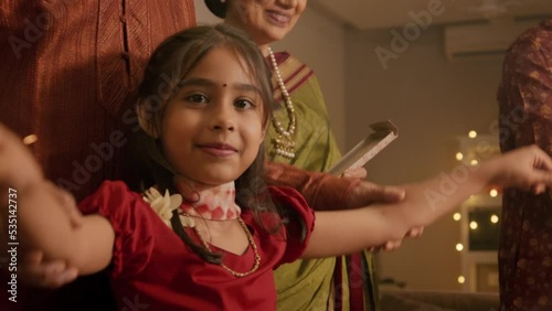 Ethnic Indian Hindu happy smiling cute young girl or female kid in traditional clothes or attire playing with firecrackers or sparklers with the help of family elders or parents during Diwali festival photo