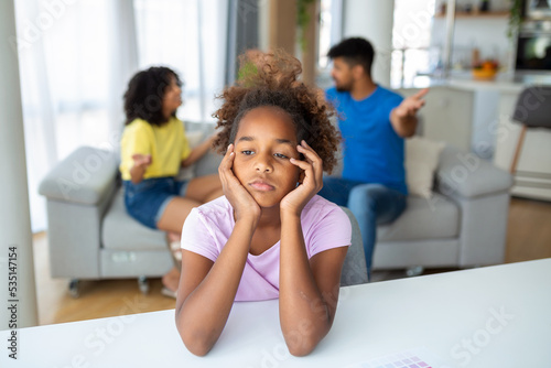 Divorce And Domestic Violence. Portrait of upset African American daughter looking through the window while her angry parents fighting in the background, depressed child feeling lonely © Graphicroyalty