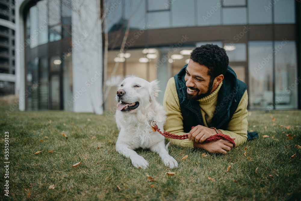 Happy young man resting with his dog outdoors in city park, during cold autumn day. Happy young man resting with his dog outdoors in city park, during cold autumn day.