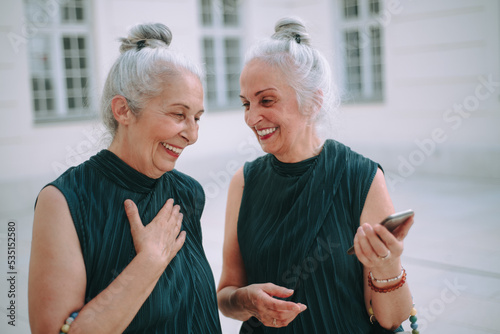 Happy senior twins in same clothes talking and walking in city. photo