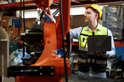 factory worker or engineer holding a laptop computer and controlling robot machine in the factory