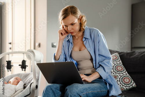 Young white mother using gadgets while spending time with her baby